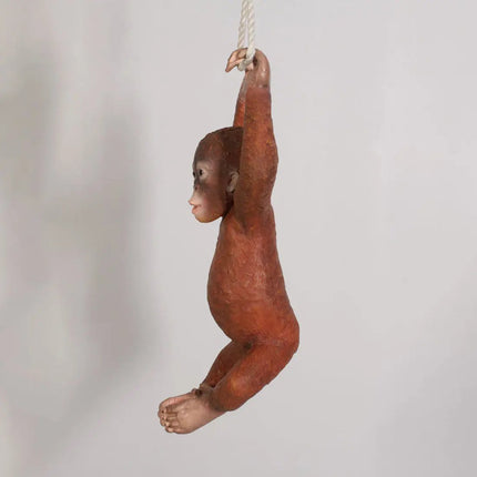 Bronze sculpture of a monkey hanging from a rope against a plain background
