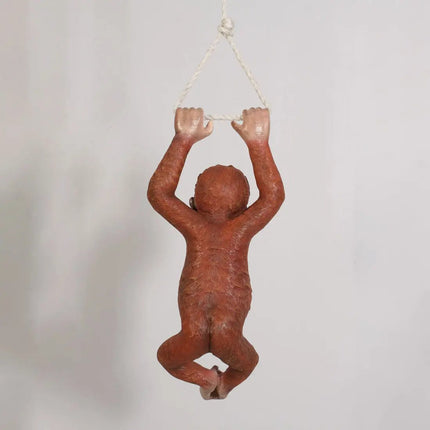 Terracotta monkey figurine hanging from a string on a light gray background