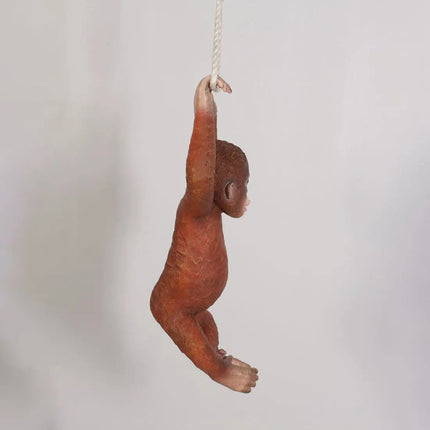 Wooden monkey ornament hanging on a string against a light gray background