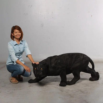 Woman kneeling next to a large black panther statue on a plain background