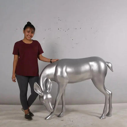 Woman standing next to Metallic silver deer sculpture on a neutral background